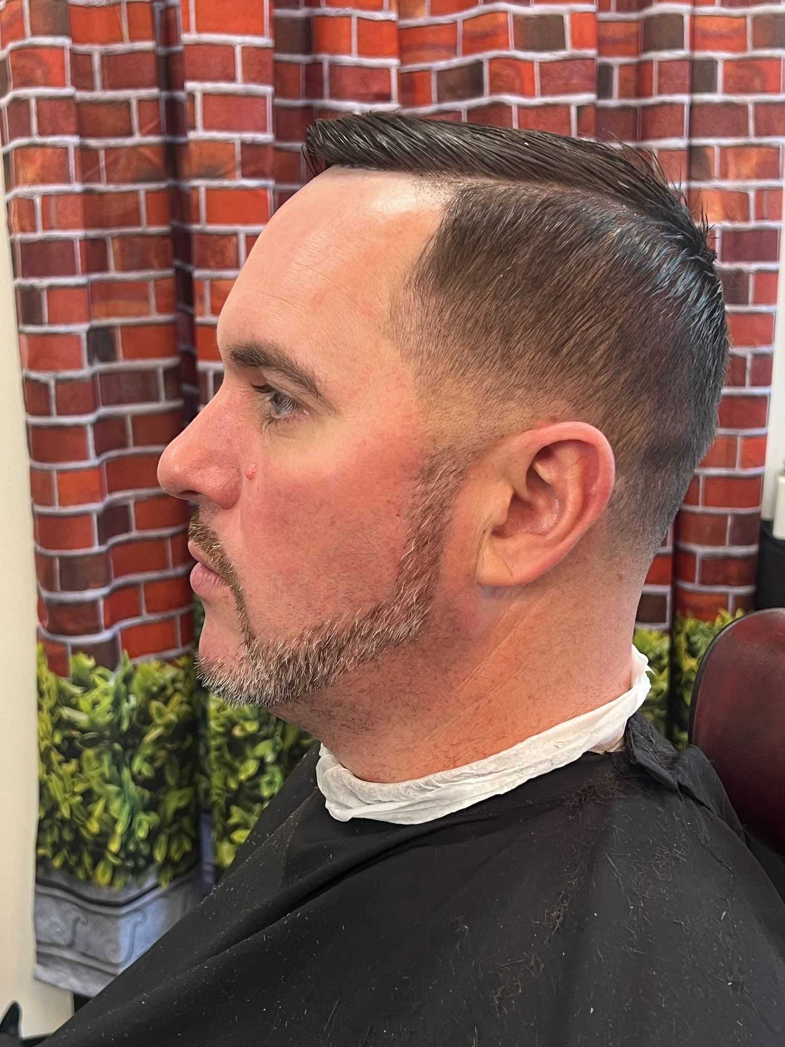 A man with a fresh haircut and groomed beard sitting in a barber chair.
